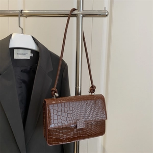 Dark brown crocodile embossed square bag with metal clasp hanging on a metal rack