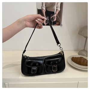 Close-up of black glossy shoulder bag with dual front pockets and vintage metal buckles