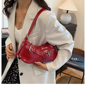 Red patent leather crescent moon armpit bag with metal eyelets on white suit background