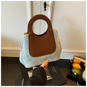 Detail of blue denim bucket bag with silver studs and round brown leather handle