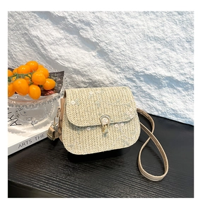 Close-up of white floral embroidery and gold metal clasp on a straw saddle bag
