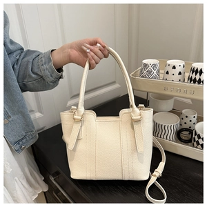 Detail of cream lychee leather texture and golden metal hardware on a stylish tote bag