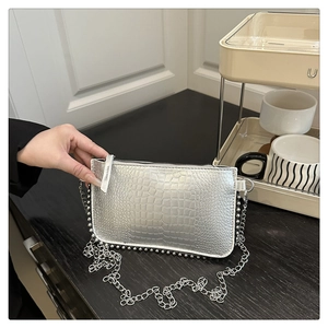 Detail of silver crocodile pattern crossbody bag with metallic chain and bead fringe