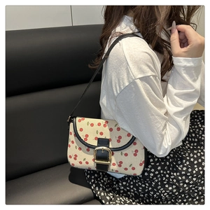 Close-up of beige cherry print handbag with black leather straps and gold horsebit detail