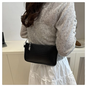 Detail of black crocodile texture shoulder bag with silver chain and beaded trim edges