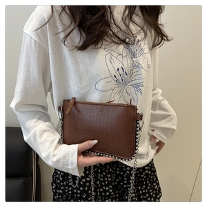 Detail of brown crocodile pattern shoulder bag with silver chain strap and metal rivets