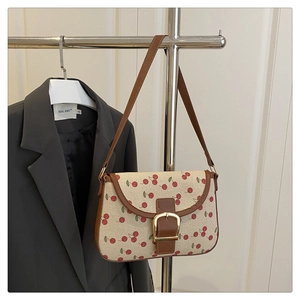 Detail of canvas cherry print bag with brown leather trim and large gold metal buckle