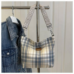 Detail of blue and yellow plaid canvas tote with a brown leather FASHION label and woven strap