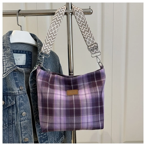 Detail of purple plaid tote bag showing wide geometric strap and brown leather patch