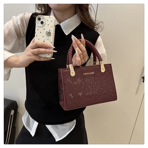 Detail of burgundy snakeskin crossbody bag with woven handle and gold hardware