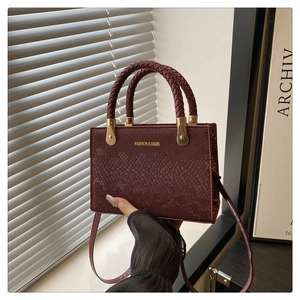 Detail of burgundy snakeskin leather tote bag with woven handles and gold metal hardware
