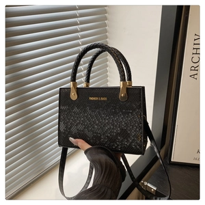 Detail of black faux snake skin texture handbag with woven handle and gold metal hardware