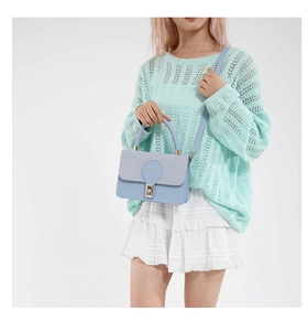 Detailed view of light blue leather handbag featuring a woven flap and gold metal clasp