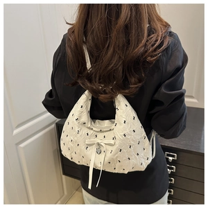 Detail of white pleated shoulder bag with black patterns and a silver heart charm