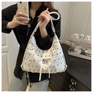 Detail of white pleated shoulder bag with black bow embroidery and heart pendant