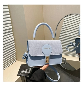 Dettaglio della borsa quadrata celeste con patta in tessuto e chiusura rotante dorata