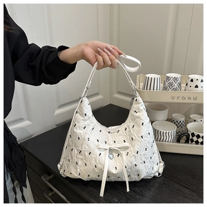 Detail of white pleated tote bag with black patterns and heart-shaped silver pendant
