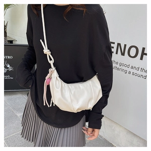 Detalle de bolso plisado blanco crema con correa anudada y colgante de fresa dulce