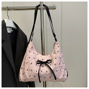 Detail of pink crinkled shoulder bag featuring black bow embroidery and heart pendant
