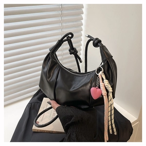 Detalle de bolso negro plisado tipo dumpling con asa de nudo y dije de corazón