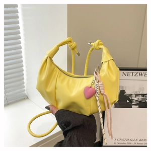 Detalle de bolso medialuna plisado amarillo con colgante de corazón y nudo
