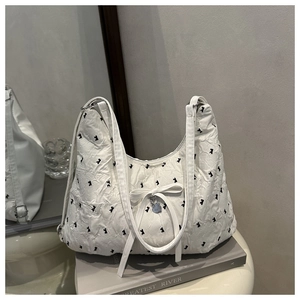 Close-up of white pleated shoulder bag featuring black bow patterns and silver heart charm
