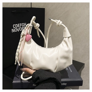 Detalle de bolso medialuna plisado blanco con colgante de corazón rosa y borla