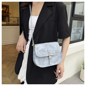 Detail of light blue saddle bag with golden clasp worn over a black blazer