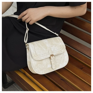 Detailed close-up of a vintage cream saddle bag with adjustable strap on a wooden bench