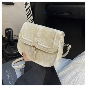 Close-up of cream saddle bag with gold clasp and adjustable strap in car interior