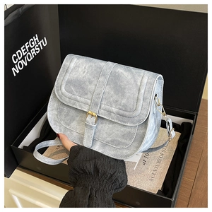 Detail view of a light blue vintage saddle bag with gold buckle in a gift box