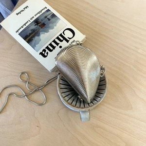 Chic silver seashell-shaped mini chain bag on a wooden table with coffee and books
