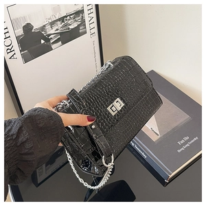 Detail of black crocodile texture bag with silver twist lock and metal chain strap