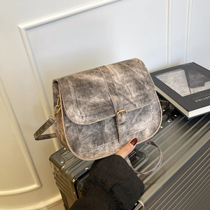 Retro taupe saddle shoulder bag with vintage metal buckle on grey textured suitcase