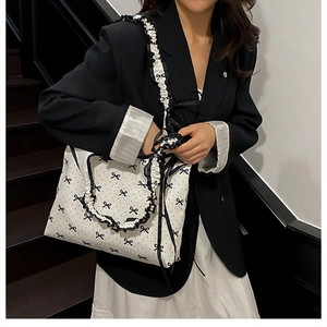 Detail of white canvas tote with black ruffle trim, bow prints, and pleated shoulder strap