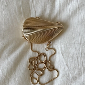 Macro shot of gold shell evening clutch with metallic radial texture and long chain strap