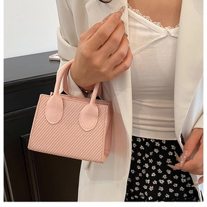 Detail view of pink mini handbag with woven texture held by model in white suit