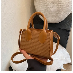 Detail of caramel brown woven leather crossbody bag with dual top handles and strap