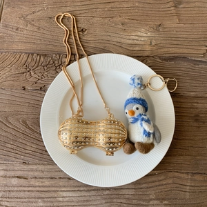 Pochette a forma di arachide con strass e catena dorata su piatto bianco e legno
