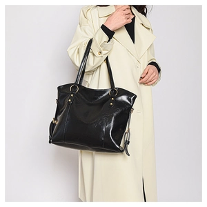Close-up of black glossy leather tote bag with dual handles on a beige trench coat