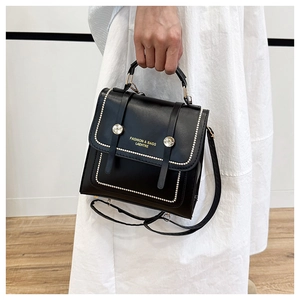 Fashionable black leather handbag with metallic buckles shown on model in white outfit