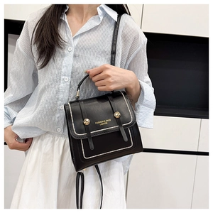 Close-up of black leather handbag featuring gold logo and white beaded edge detailing