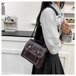 Detail of dark brown leather crossbody bag with white stitching and gold hardware buckle