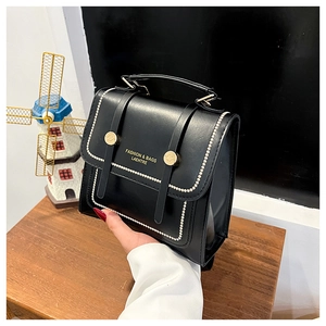 Detail of black faux leather handbag with pearl trim and gold buckle accents