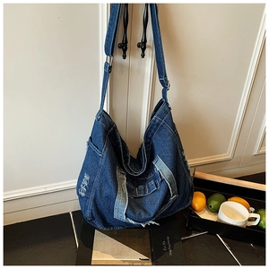 Détail d'un sac messager en denim bleu suspendu à la poignée de porte avec accessoires