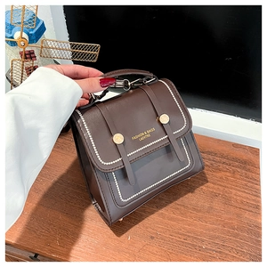Detail of dark brown leather handbag with contrast stitching and golden logo on wood background