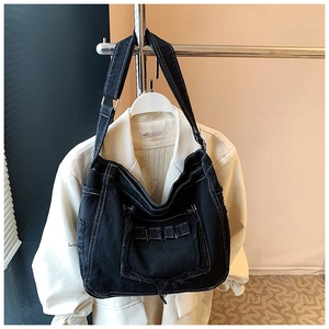 Gros plan sur un sac messager en denim noir avec surpiqûres blanches et bords effilochés