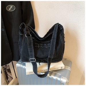 Détail du sac messager en denim noir avec coutures blanches et bords à franges