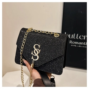 Close-up of black glitter crossbody bag with gold metal S-logo and fringe details