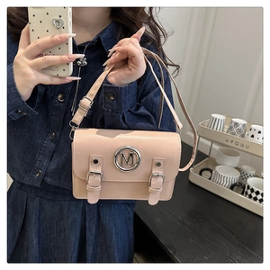Détail du sac à bandoulière en cuir rose avec logo M argenté tenu par un mannequin en jean